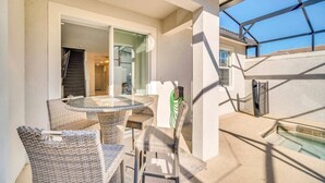 Une terrasse extérieure avec une table en verre et des chaises en osier, une piscine et un espace abrité offrant une vue sur le ciel.