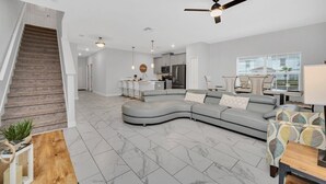 Un salon moderne avec un canapé gris aux lignes courbes, une table basse en bois et un escalier menant à un autre niveau.