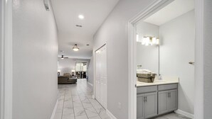 Un couloir doté d’un sol en marbre qui mène à une salle de bain avec un meuble-lavabo et un grand miroir.