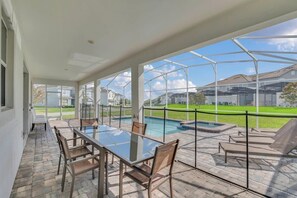 Un patio couvert avec une table et des chaises en verre, une piscine et une vue sur un quartier résidentiel.