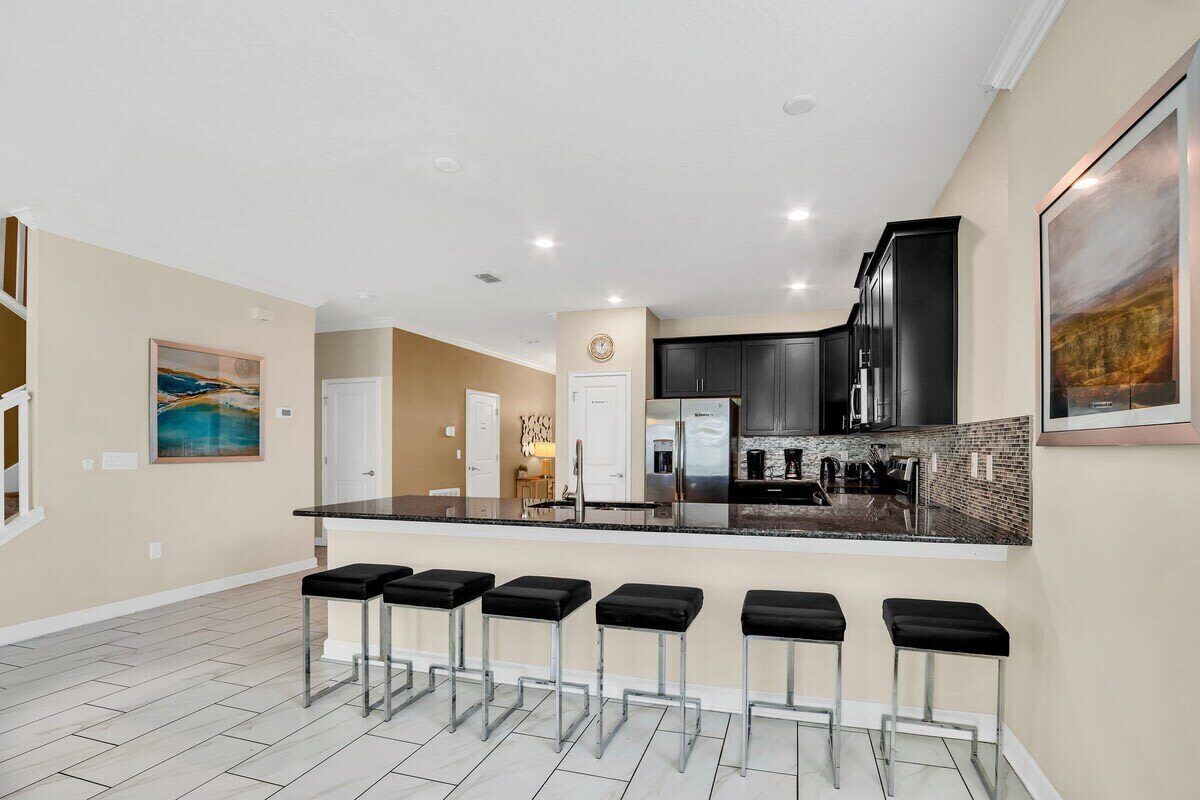 A modern kitchen with a central island, bar stools, and a dining area.