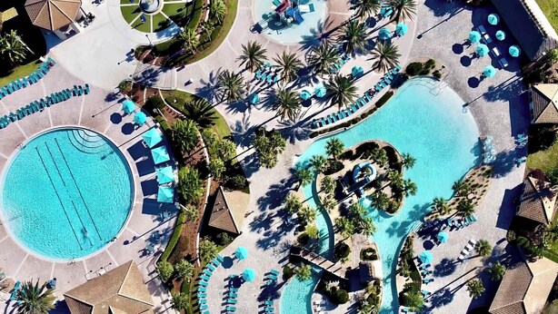 Eine Luftaufnahme eines Resorts mit mehreren Schwimmbecken, Liegestühlen und Palmen.