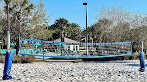 A beach volleyball net with blue padding, surrounded by sand and palm trees. - Mickey | South Pool & Spa | Game Room | Disney 9022 (Davenport)