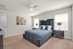 A bedroom with a large bed, a ceiling fan, a nightstand, and a window with blinds.