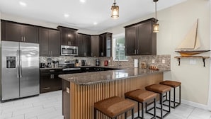 A modern kitchen with dark wood cabinets, stainless steel appliances, a granite island with bar stools, and pendant lighting. - Harry Potter | Star Wars | Pool & Spa | Disney 9026 (Davenport)
