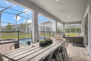 A covered patio with a pool, outdoor seating, and a view of the neighborhood.