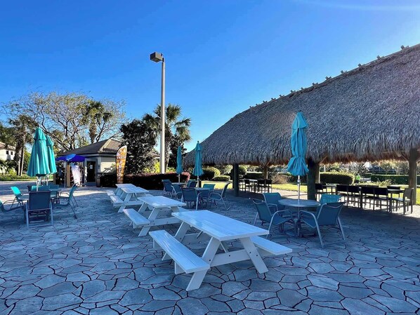 An outdoor seating area with tables and chairs, a thatched-roof structure, and a street lamp.