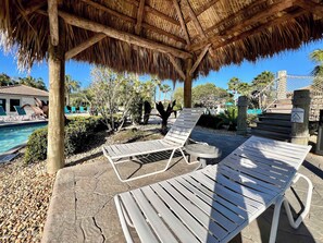 A poolside area with wooden lounge chairs, a thatched roof structure, and a pool.