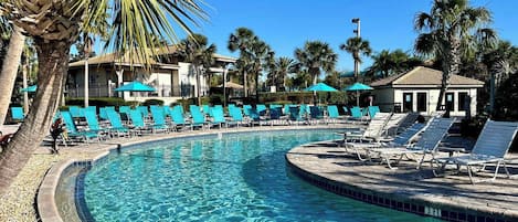A pool area with clear blue water, surrounded by lounge chairs and palm trees.