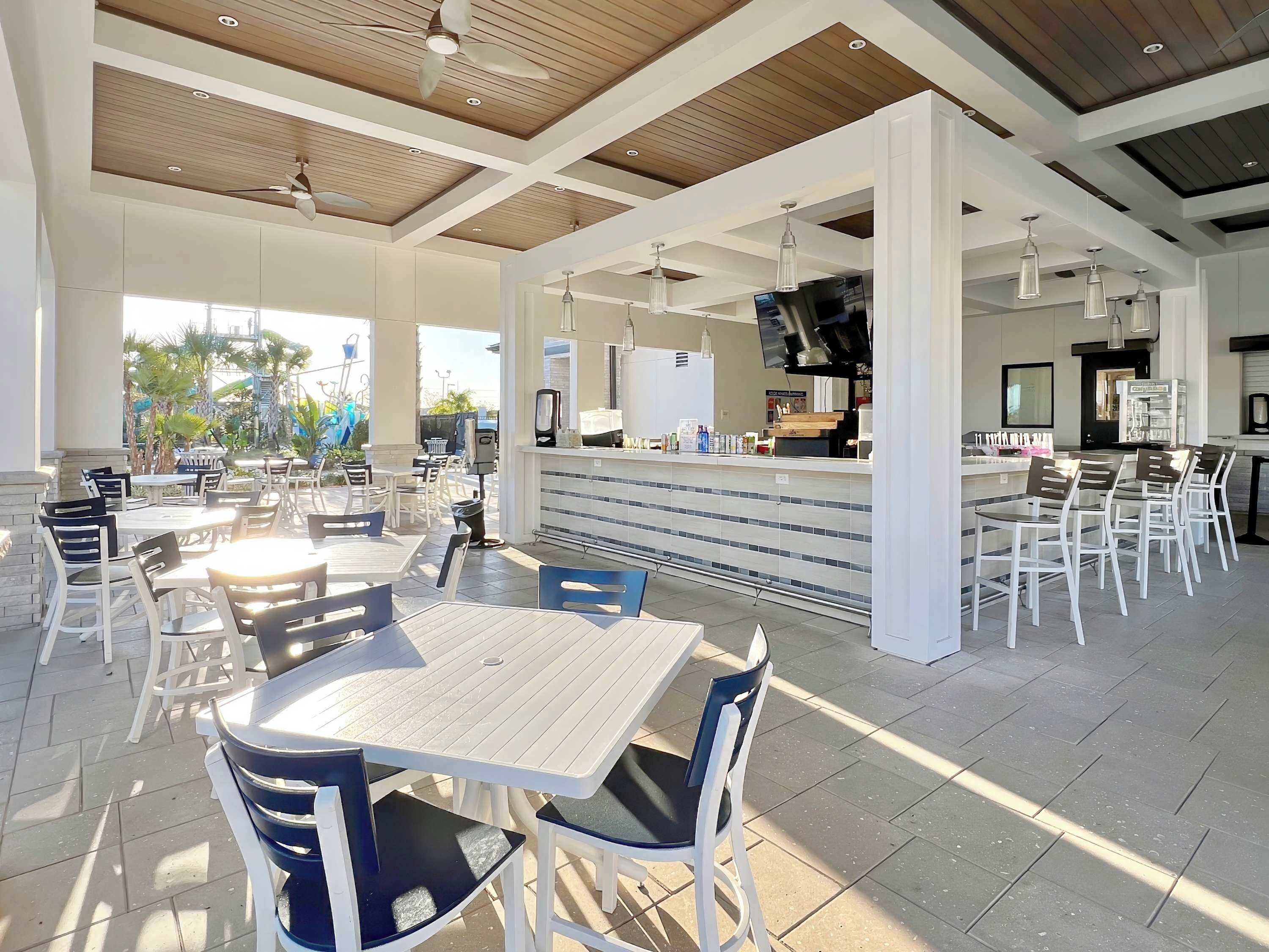 A spacious indoor dining area with multiple tables and chairs, a counter with a coffee station, and a ceiling fan.