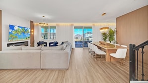 Una sala de estar moderna con un sofá modular, un comedor con mesa de madera y sillas blancas, y una escalera con barandilla negra.