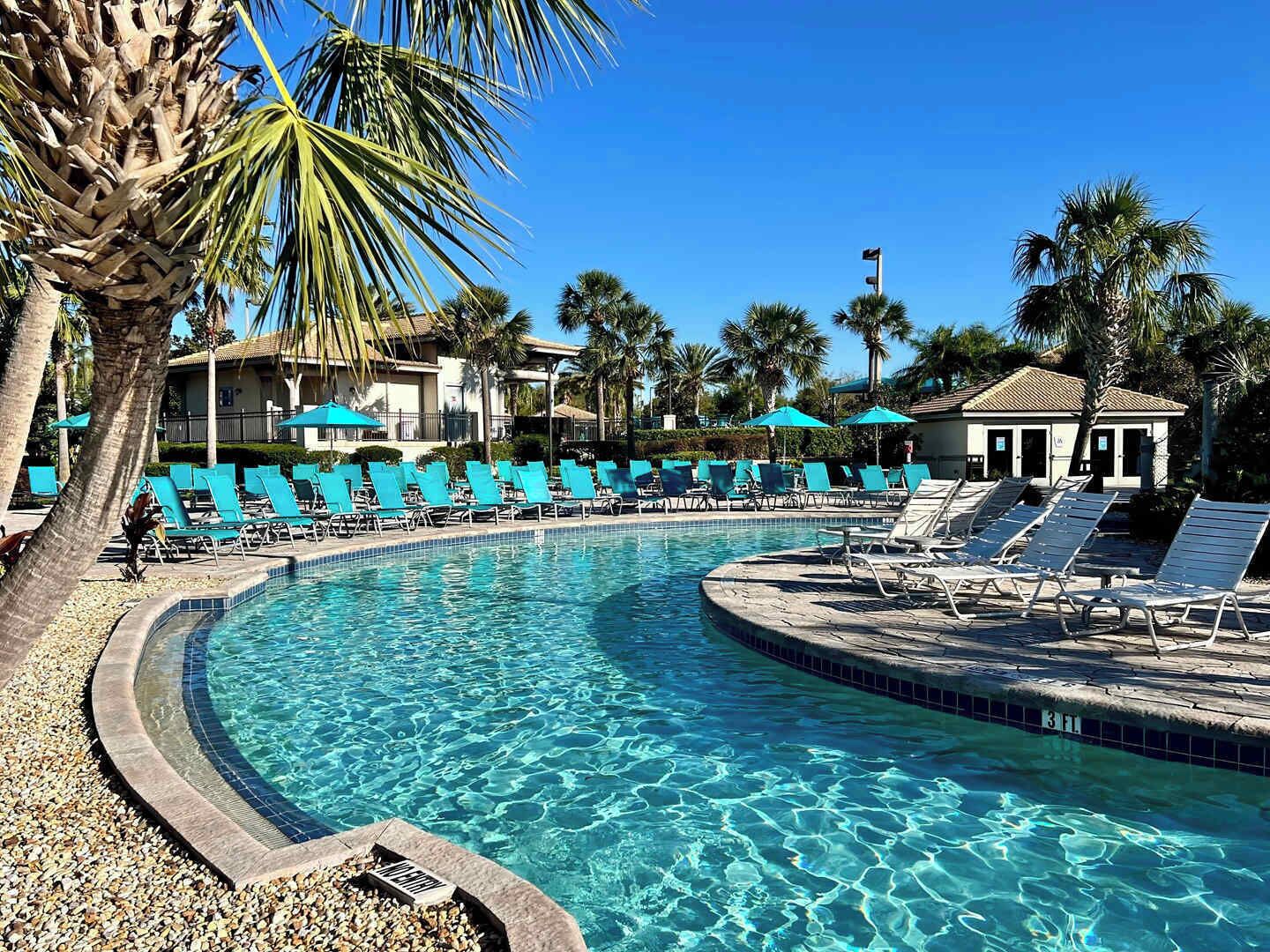 A pool area with clear blue water, surrounded by lounge chairs and palm trees.
