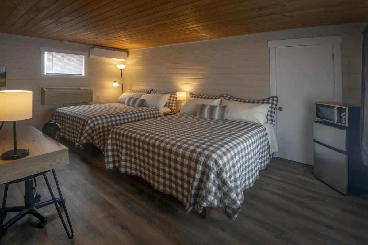 Una habitación con dos camas, un escritorio, una silla, una lámpara, un microondas y una puerta.