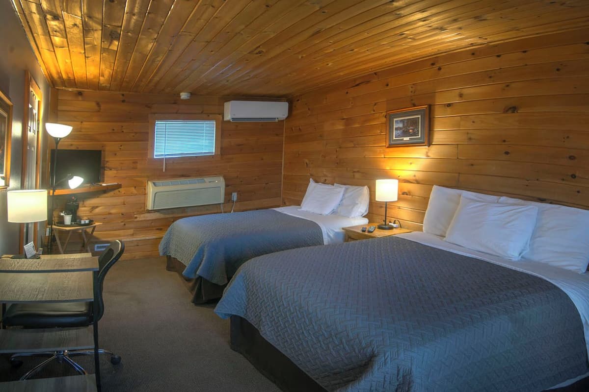 Una habitación tipo cabaña con dos camas, un escritorio con una silla, un televisor y una ventana con persianas.