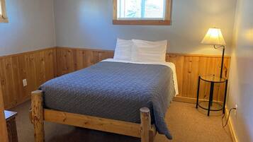 Una cama de madera con una colcha acolchada, una lámpara de noche y una ventana con persianas.