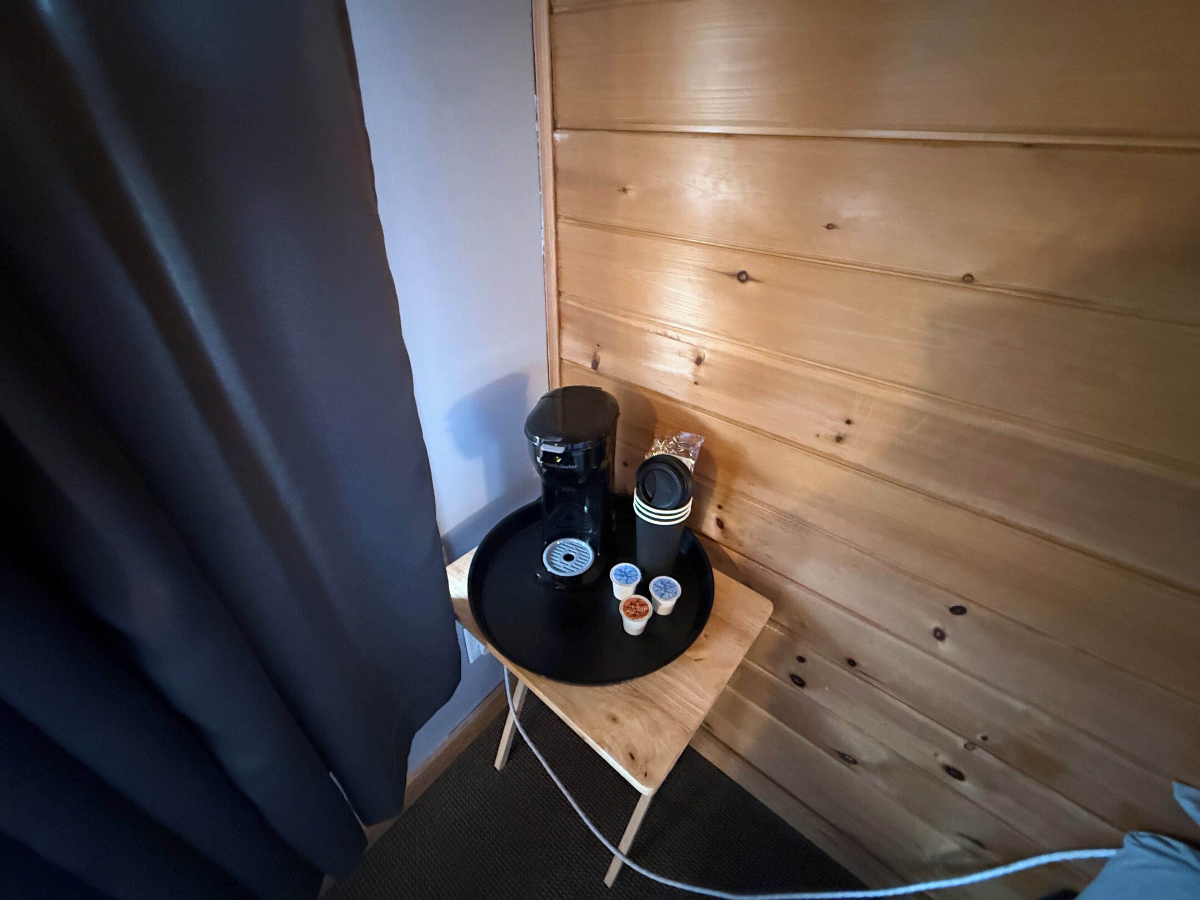 Una pequeña mesa de madera con una cafetera, una taza y un platito.