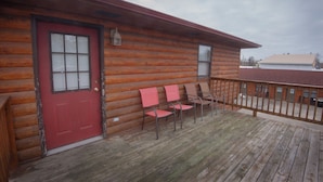 A log cabin with a red door, a porch with four chairs, and a wooden deck. - Rustic Inn (Park Rapids)