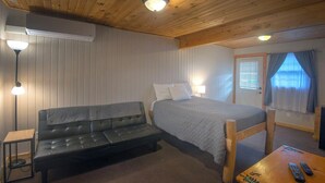 A cozy room with a bed, a sofa, a small table, and a lamp. - Rustic Inn (Park Rapids)