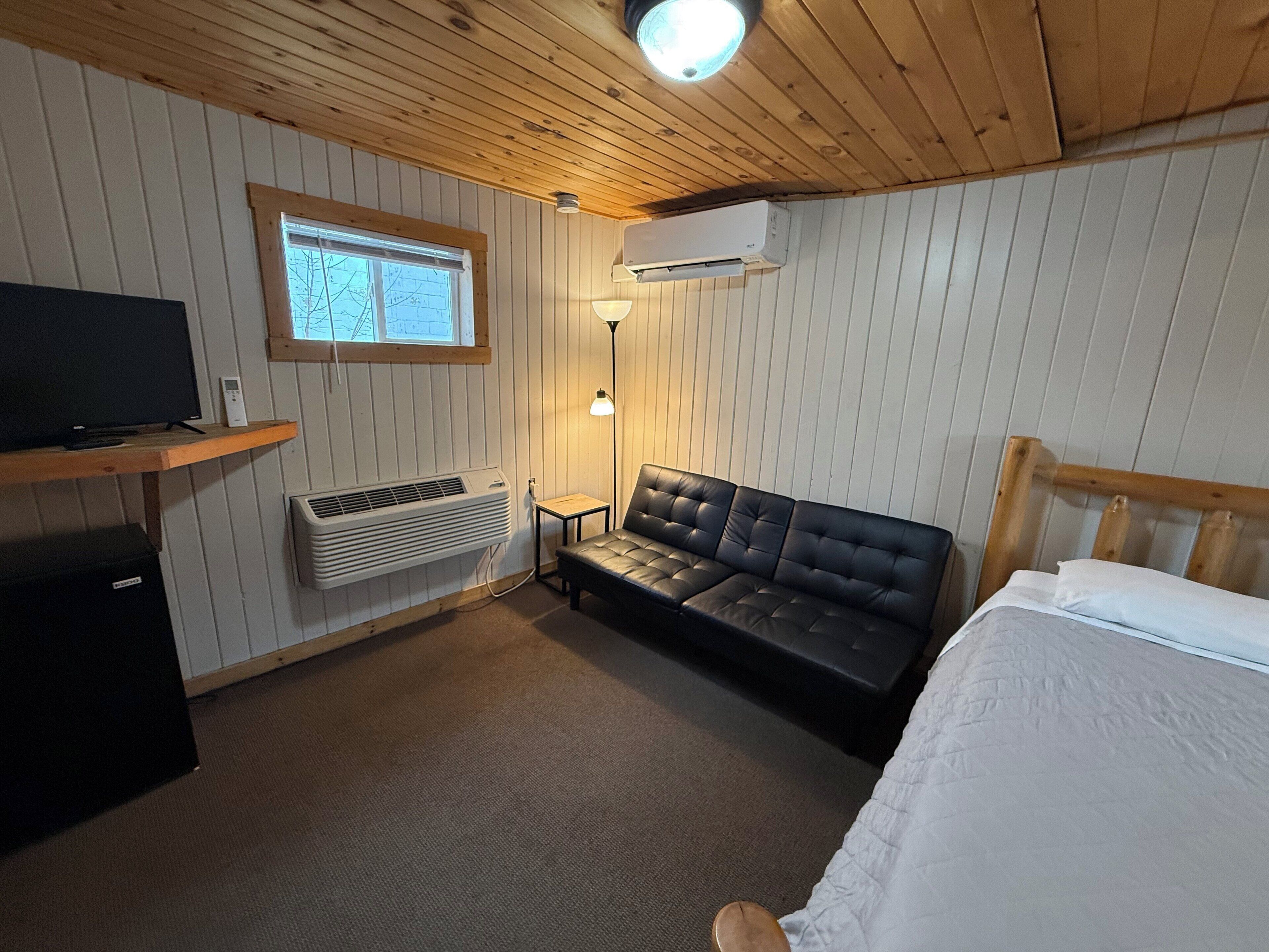 A room with a bed, a sofa, a TV, an air conditioner, a lamp, and a window.