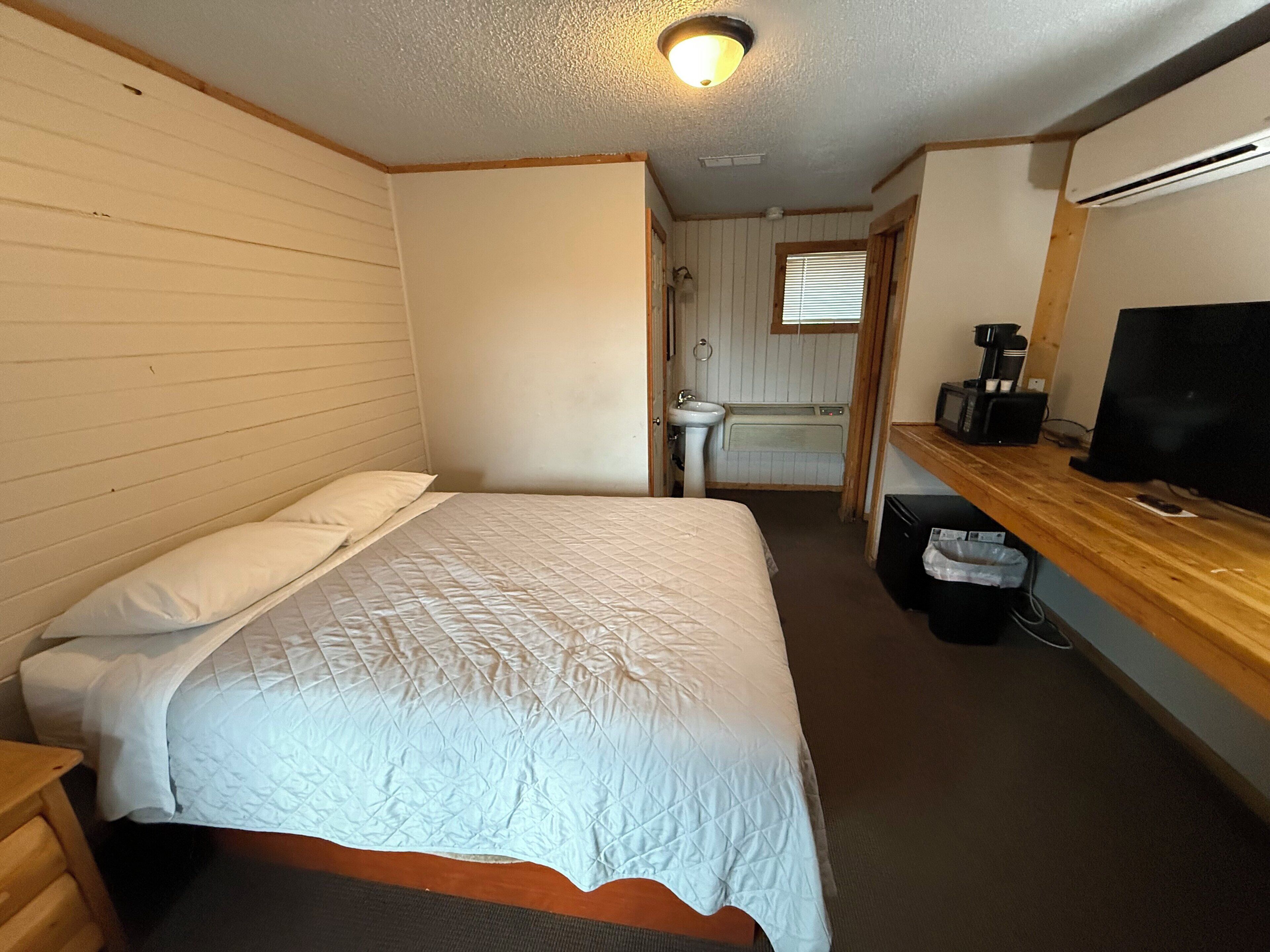 Una habitación pequeña y funcional con cama, lavamanos, espejo y televisor.