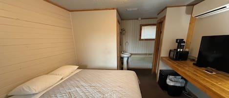 A small, compact room with a bed, a sink, a mirror, and a television.