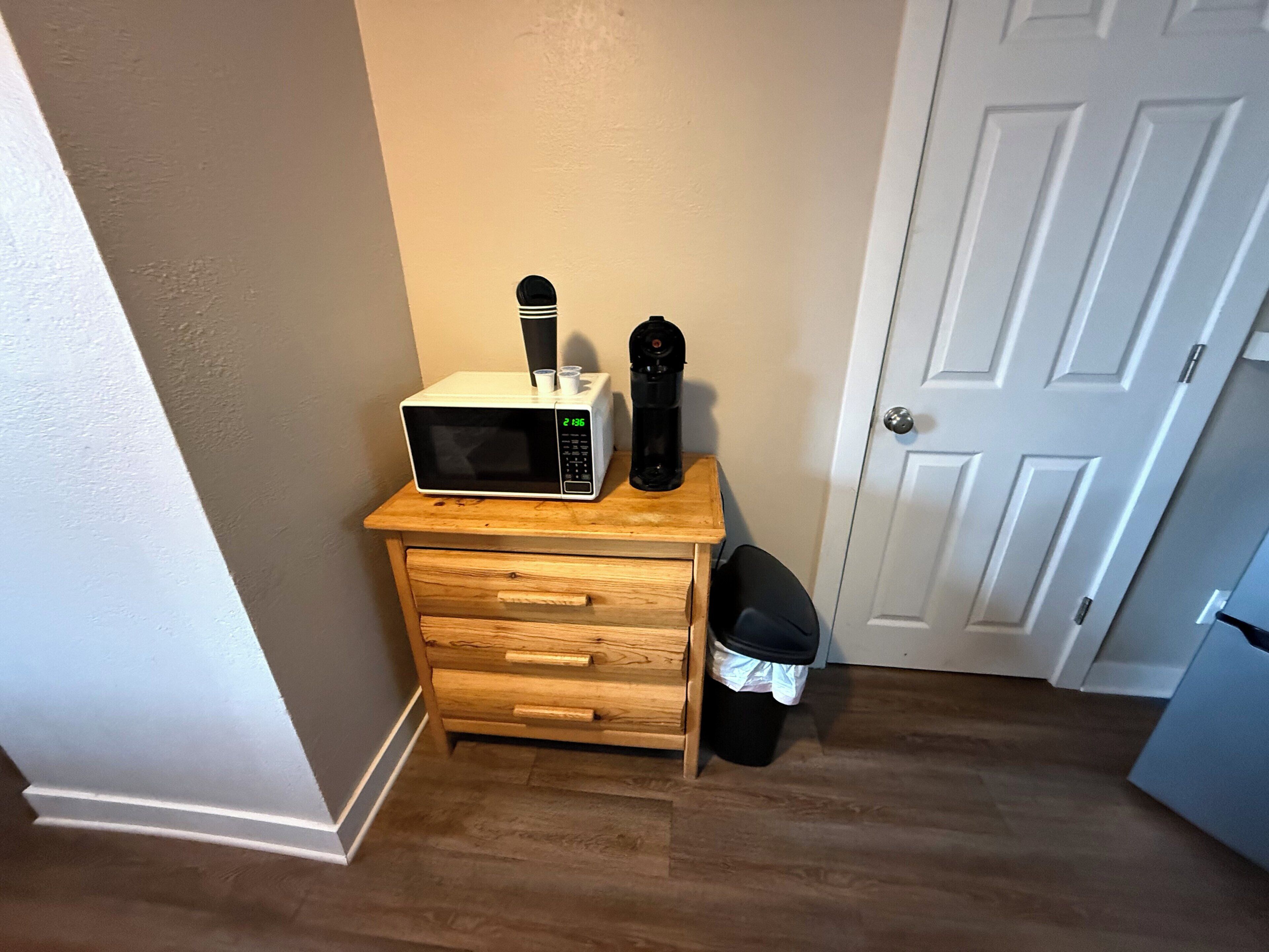 A compact kitchen with a microwave, coffee maker, and trash bin.