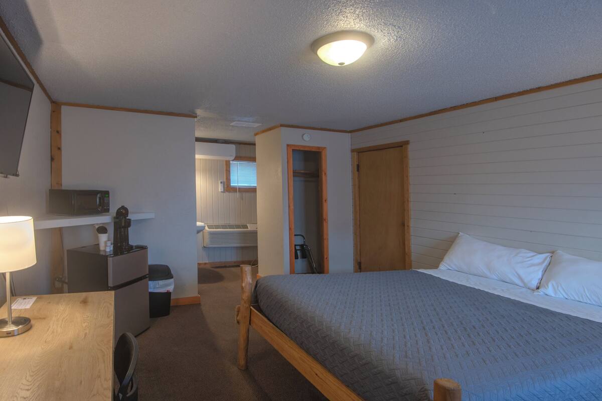 Un dormitorio con una cama, un escritorio con lámpara, un microondas y una ventana pequeña.