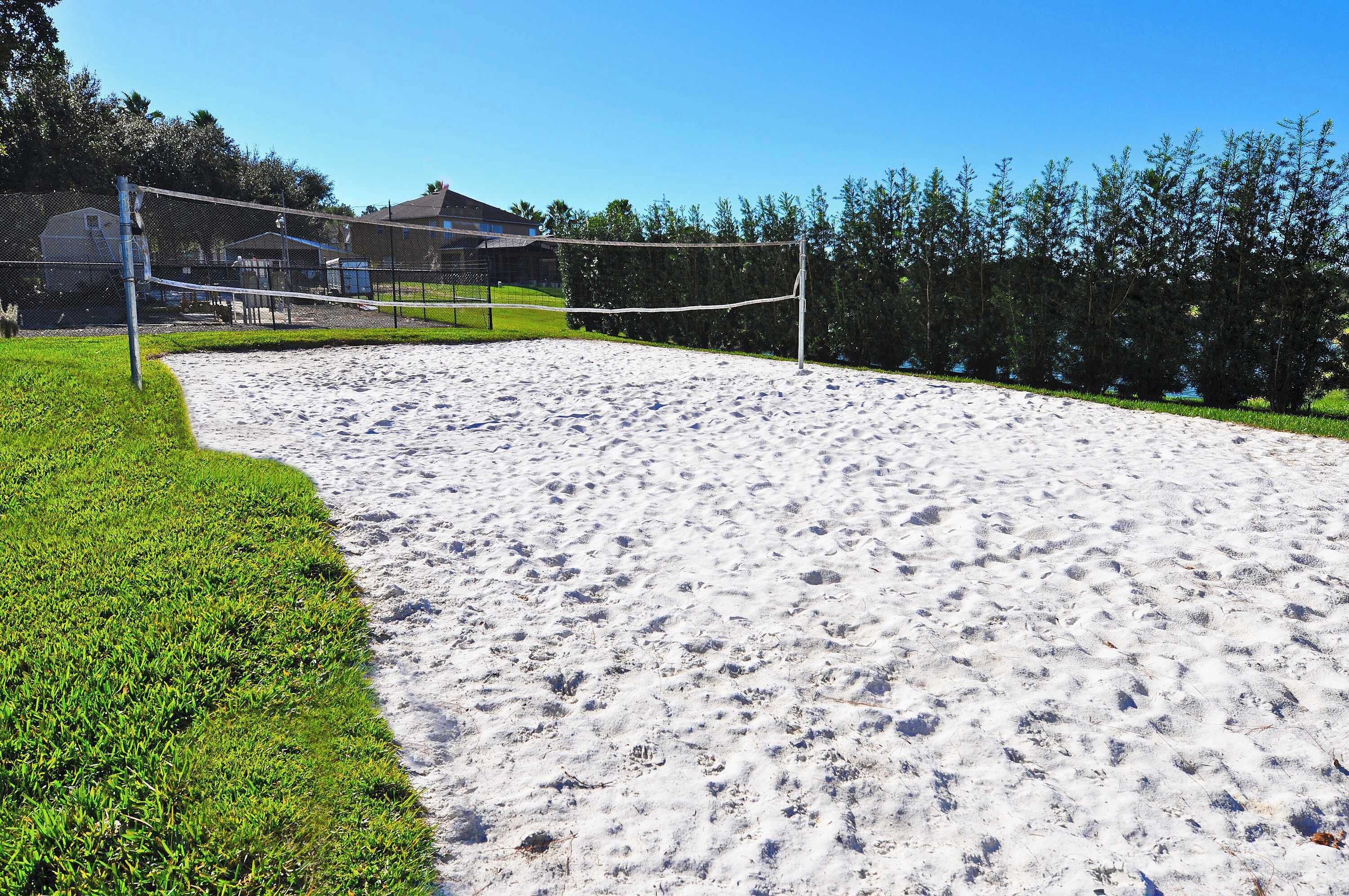 En sandvolleyspillplan med ett nät, omgiven av gräs och träd.