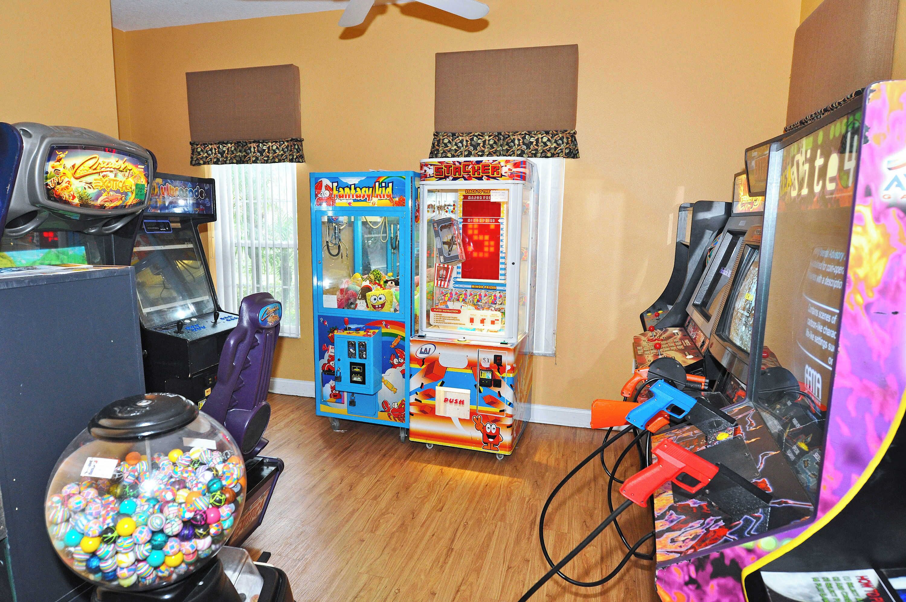 A room with arcade games, including a claw machine, a game titled 'Fantasy Kid,' and a 'Stacker' game.