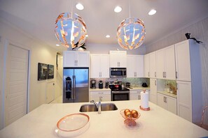 Cocina moderna con armarios blancos, electrodomésticos de acero inoxidable y dos lámparas colgantes esféricas.