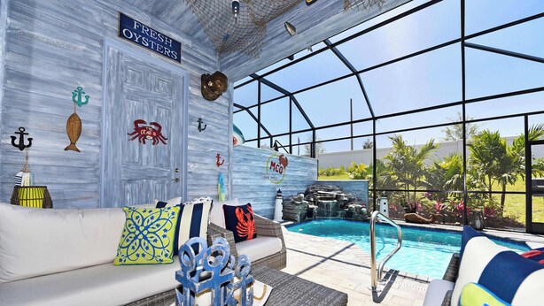 Ein Poolbereich mit einer weißen Couch, dekorativen Kissen und einem Tisch mit einem Meeresfrüchte-Zentrum.