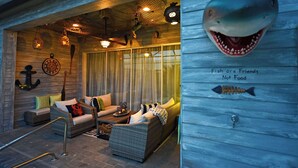 Ein maritim eingerichtetes Zimmer mit Rattanmöbeln, einem großen Fenster und einer Wanddekoration mit einem Hai.