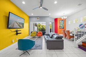A modern living room with a flat-screen TV, a ceiling fan, and a large window.