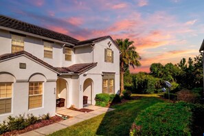 A two-story house with a covered porch, a well-maintained lawn, and a sunset sky.