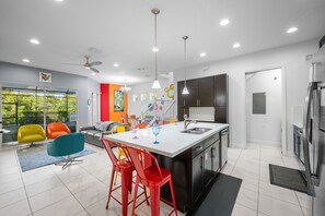 A modern kitchen with a central island, stainless steel appliances, and a dining area with colorful chairs.