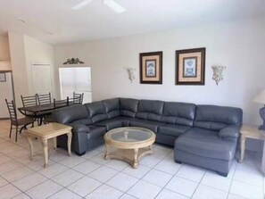 A living room with a sectional sofa, a round coffee table, and a dining area with chairs and a table.