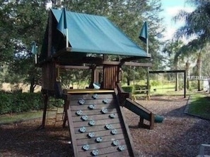 A wooden slide structure with a green roof and metal handrails, surrounded by trees and a grassy area.