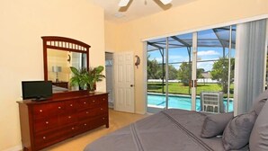 Una camera da letto con un letto grande, una cassettiera, una TV e una porta vetrata scorrevole che dà su una piscina.