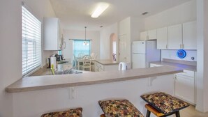 Una cocina moderna con armarios blancos, una isla central y un comedor con sillas.