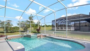 Una piscina con cerramiento de vidrio, rodeada de áreas ajardinadas con césped y árboles.