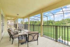 Een overdekt balkon buiten met een tafel en stoelen, en uitzicht op een groen landschap met een metalen hekwerk.