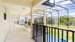 A covered outdoor area with a pool, a chair, and a view of the surrounding landscape. - Conservation View | Pool & Spa | 7 Miles Disney 203 (Davenport)