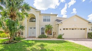 A two-story house with a garage, a well-maintained lawn, and palm trees. - Conservation View | Pool & Spa | 7 Miles Disney 203 (Davenport)