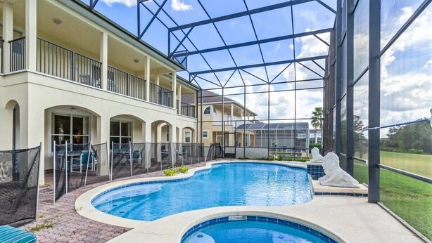 A swimming pool with a glass enclosure, a covered patio, and a view of the surrounding landscape. - Conservation View | Pool & Spa | 7 Miles Disney 203 (Davenport)