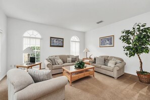 A spacious living room with two sofas, a coffee table, and a large window with arched top. - Conservation View | Pool & Spa | 7 Miles Disney 203 (Davenport)
