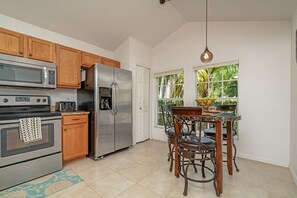 A kitchen with wooden cabinets, stainless steel appliances, a dining table with chairs, and a window with a view of greenery.