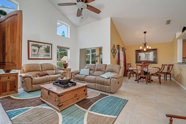 A spacious living room with two beige sofas, a wooden coffee table, and a dining area with a table and chairs.