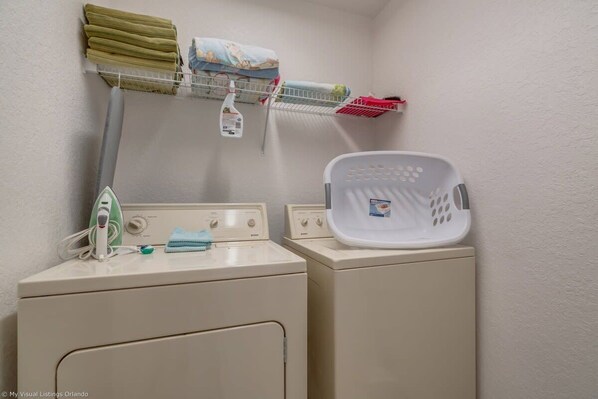A laundry area with two washing machines, a drying rack with folded clothes, a laundry basket, and a bottle of detergent.