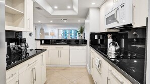 A modern kitchen with white cabinets, black countertops, and a microwave. - Sauna | Hot Tub | Skyline & Bay Views | StayCozy (Miami)