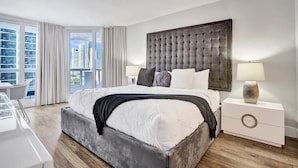 A modern hotel room with a large bed, a nightstand, a desk, and a view of the cityscape. - Sauna | Hot Tub | Skyline & Bay Views | StayCozy (Miami)